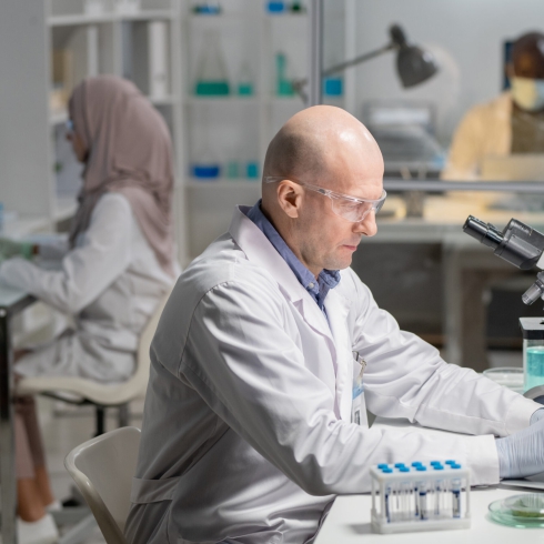 Mature serious male lab worker in gloves, whitecoat and protective eyeglasses searching for scientific information in the net
