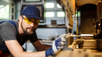Portrait of worker near metalworking machine, industrial steel factory background.