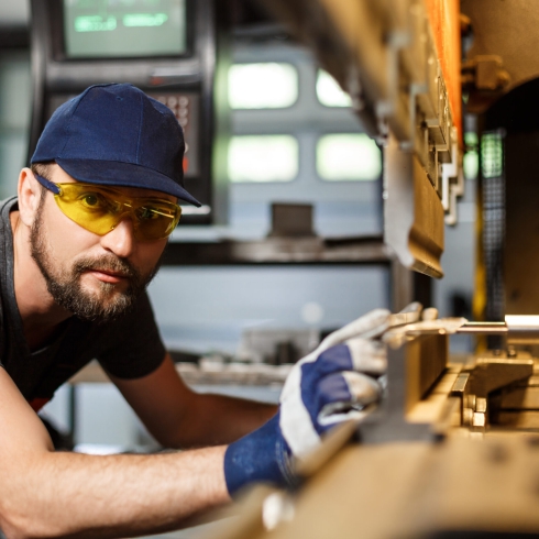 Portrait of worker near metalworking machine, industrial steel factory background.