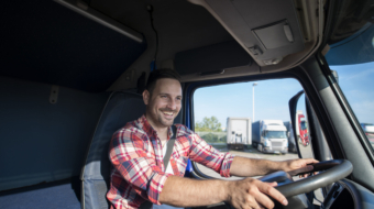 Professional truck driver in casual clothing wearing seat belt on and driving his truck to destination.