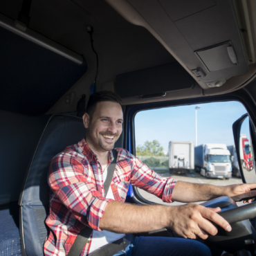 Professional truck driver in casual clothing wearing seat belt on and driving his truck to destination.